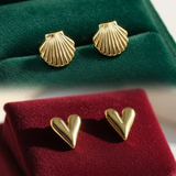 Gold shell-shaped earrings on green velvet and gold heart-shaped earrings on red velvet