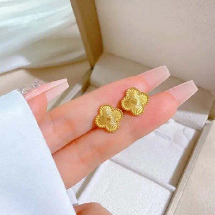 Gold flower-shaped earrings held in a hand with a white background